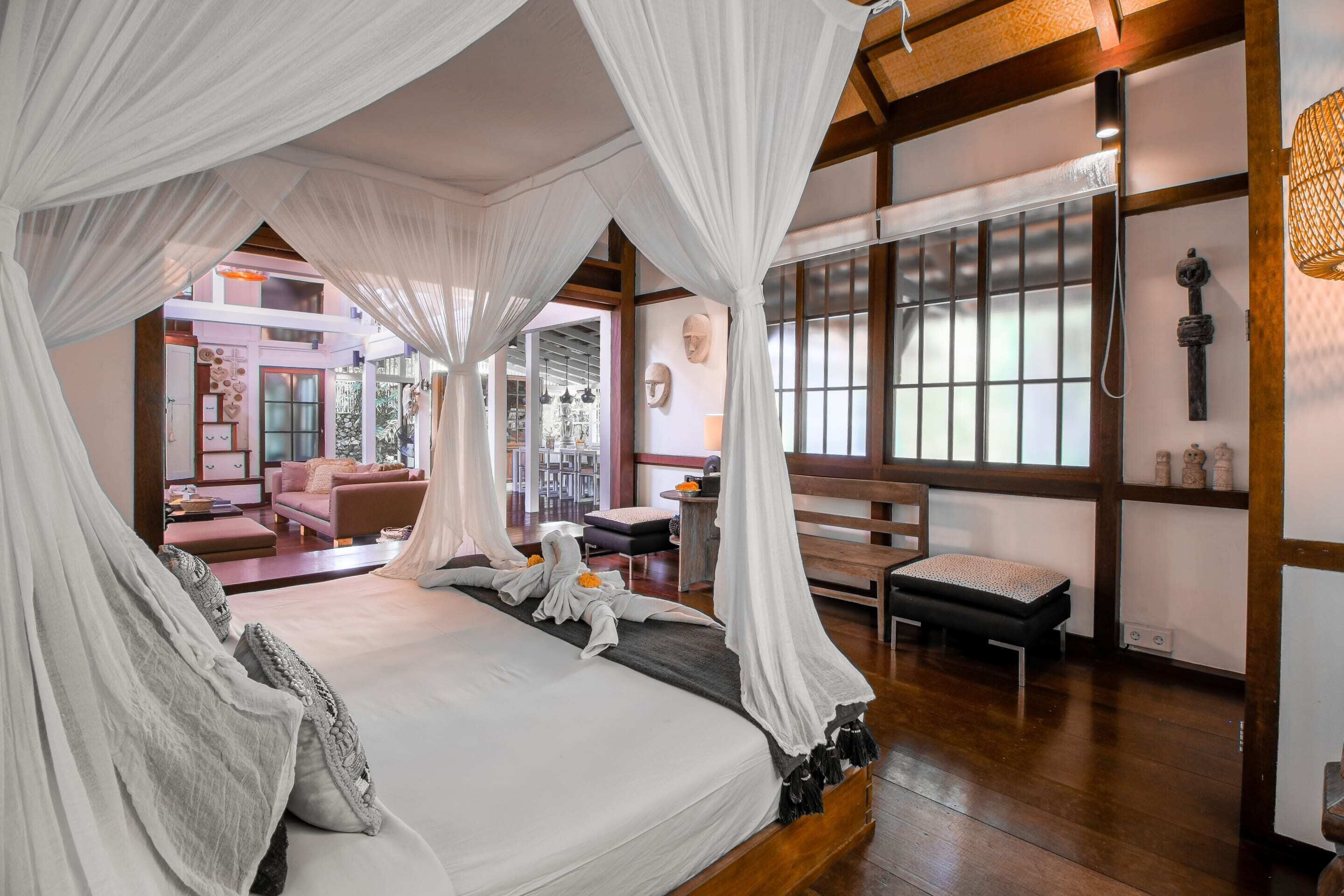 A spacious bedroom with a canopy bed, wooden flooring, and large windows.