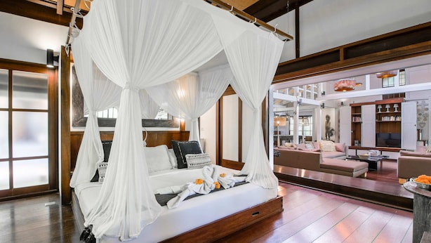 Une chambre spacieuse dotée d’un grand lit à baldaquin, d’un coin salon avec des canapés et d’un téléviseur placé à l’arrière-plan.