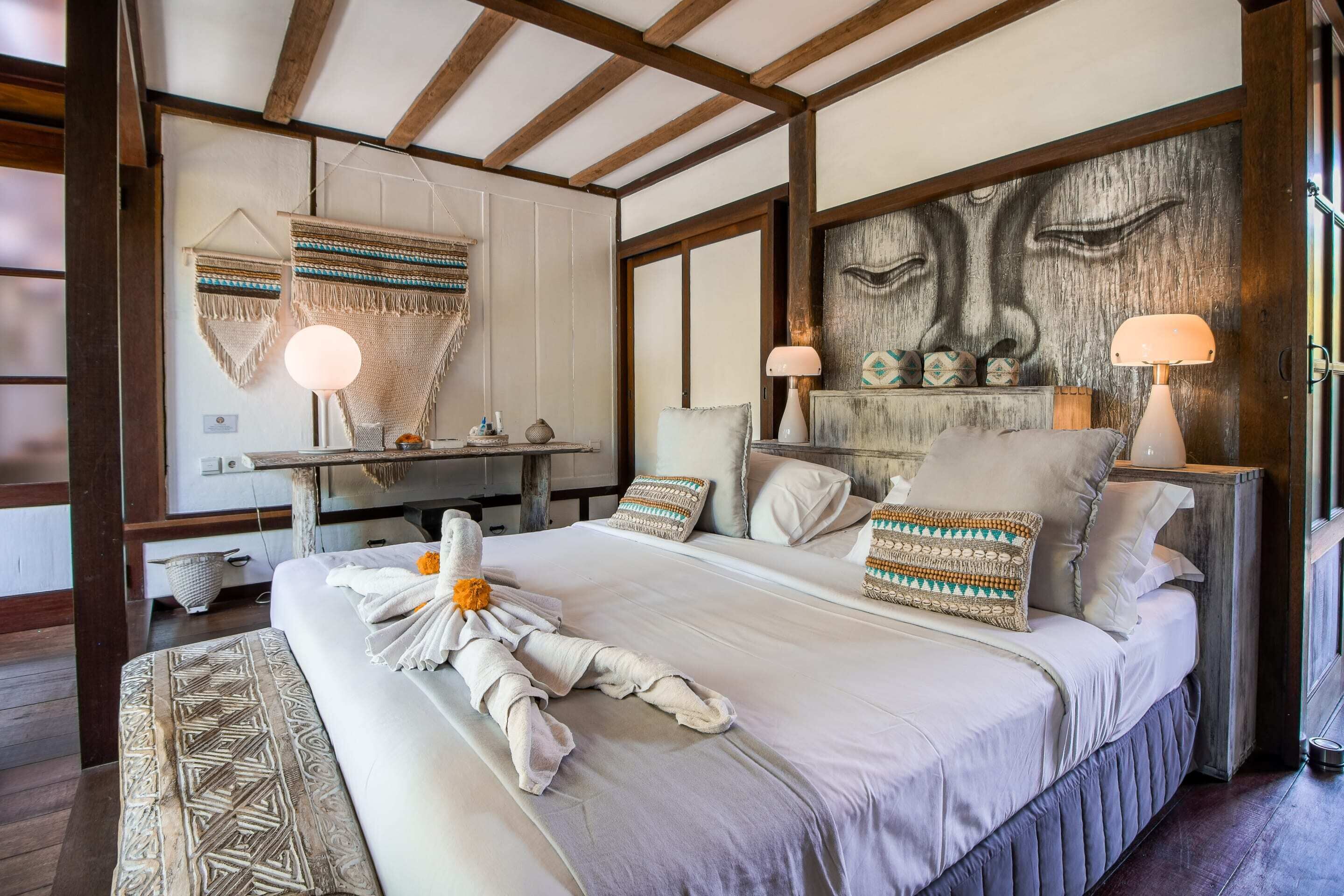 Une chambre élégamment aménagée, dotée d’un grand lit, de nombreux oreillers, d’une tête de lit ornée d’une œuvre d’art, de lampes de chevet et d’une décoration murale.