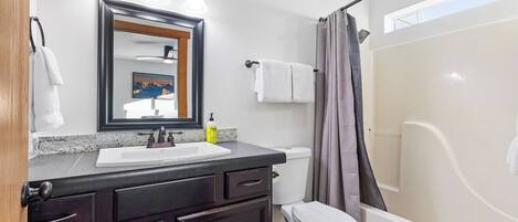 Un baño con lavamanos, espejo, inodoro y cortina de ducha.