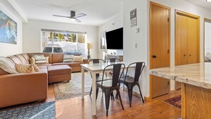 A modern living room with a sofa, dining table, and chairs. There is a TV mounted on the wall and a ceiling fan. - Cozy Condo Located  Minutes from the Biggest Skiing in America (Big Sky)