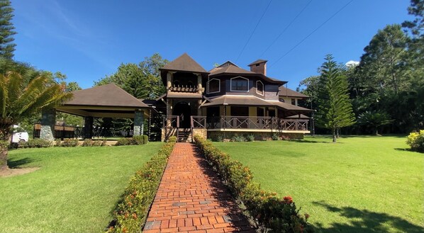 Step into a serene country retreat with a charming front porch and patio area, surrounded by a beautifully manicured lawn and lush trees.