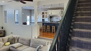 A spacious living area with a sofa, a ceiling fan, and a staircase leading to a kitchen area with bar stools.