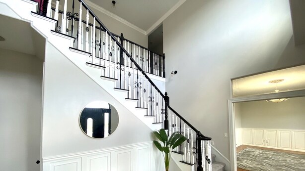 A staircase with white railings and black balusters, a round mirror, a bench, and a potted plant.