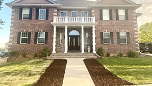 A two-story brick house with a front porch, a driveway, and a well-maintained lawn.