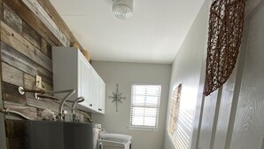 Ett kompakt kök med kylskåp, tvättmaskin och ett fönster med persienner.
