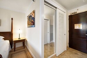 A hotel room with a bed, bedside table with a lamp, a painting on the wall, and a dark wooden door. - Beachfront Resort, Tropical pools with cascading waterfalls, Restaurants on site (Lihue)
