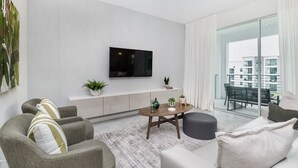 Ein modernes Wohnzimmer mit flachbildfernseher an der Wand, einem weißen Lowboard mit Pflanzen und einem Essbereich mit Glastisch und Stühlen.