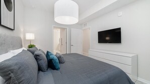 Ein modernes Schlafzimmer mit einem großen Bett, einem flachbildfernseher an der Wand und einem weißen Konsolentisch.
