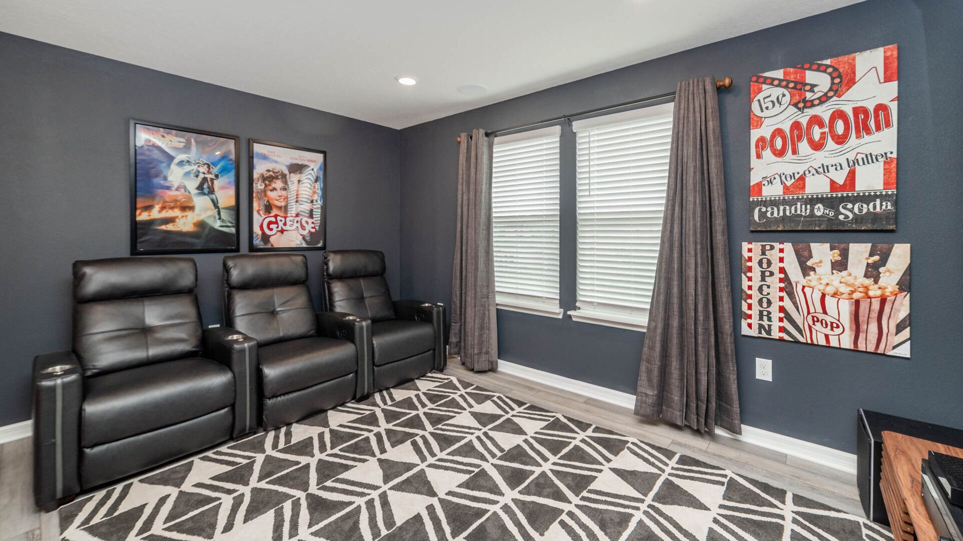 A home theater room with three black leather recliners, a patterned rug, and movie posters on the wall.