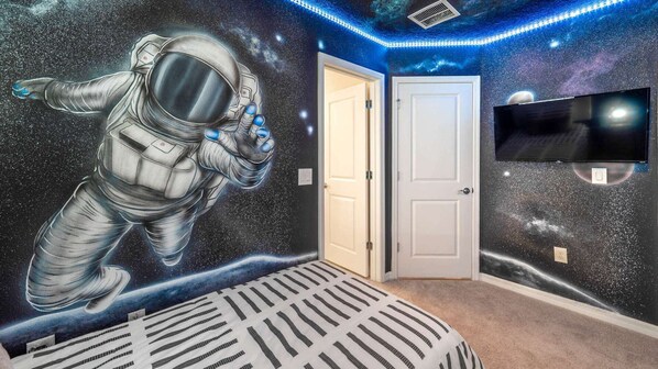 A room with a space-themed mural, a television, and a patterned rug.