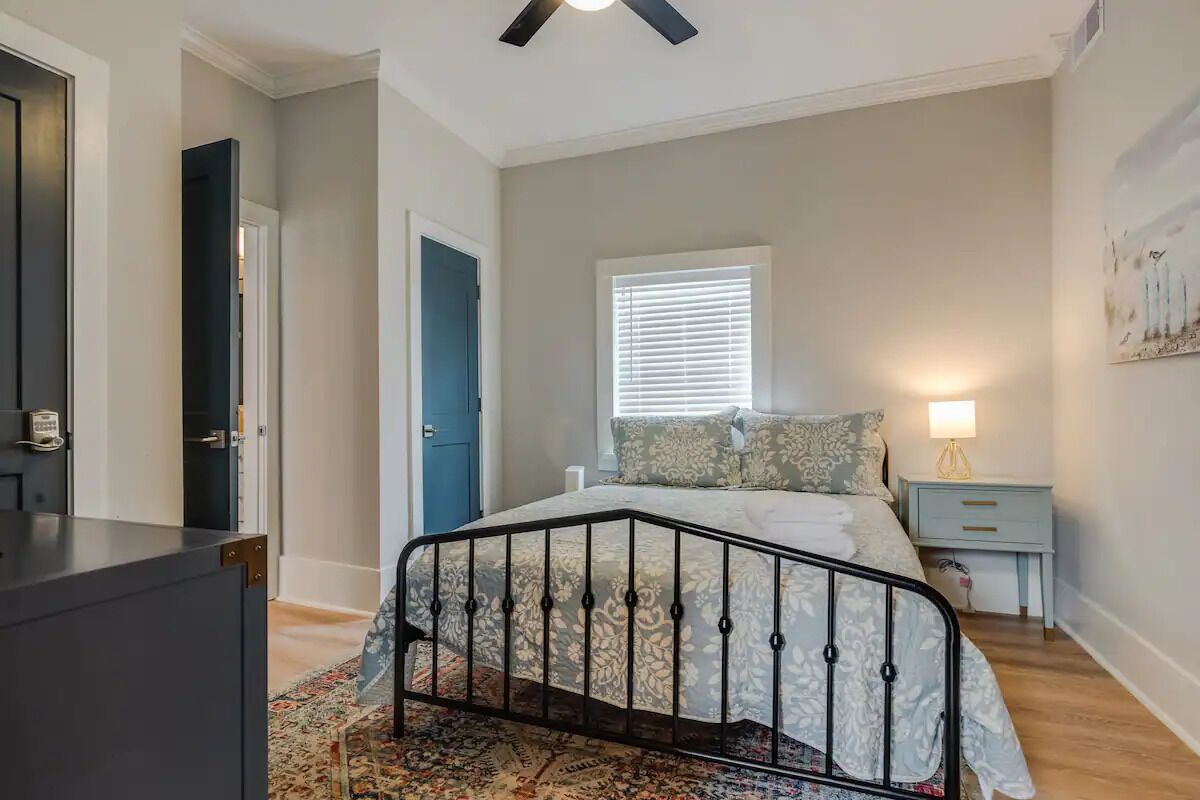A bedroom with a bed, a nightstand, a lamp, a window with blinds, and a ceiling fan.