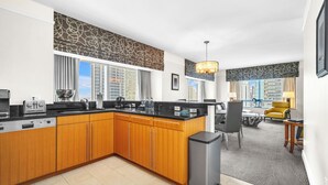 Een moderne keuken met houten kastjes, een zwart aanrecht en een inbouwfornuis. Er is een eethoek met een gele stoel en een tafel.
