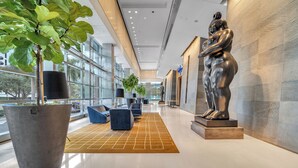 Een moderne lobby met een grote plantenbak, zithoek en een standbeeld.