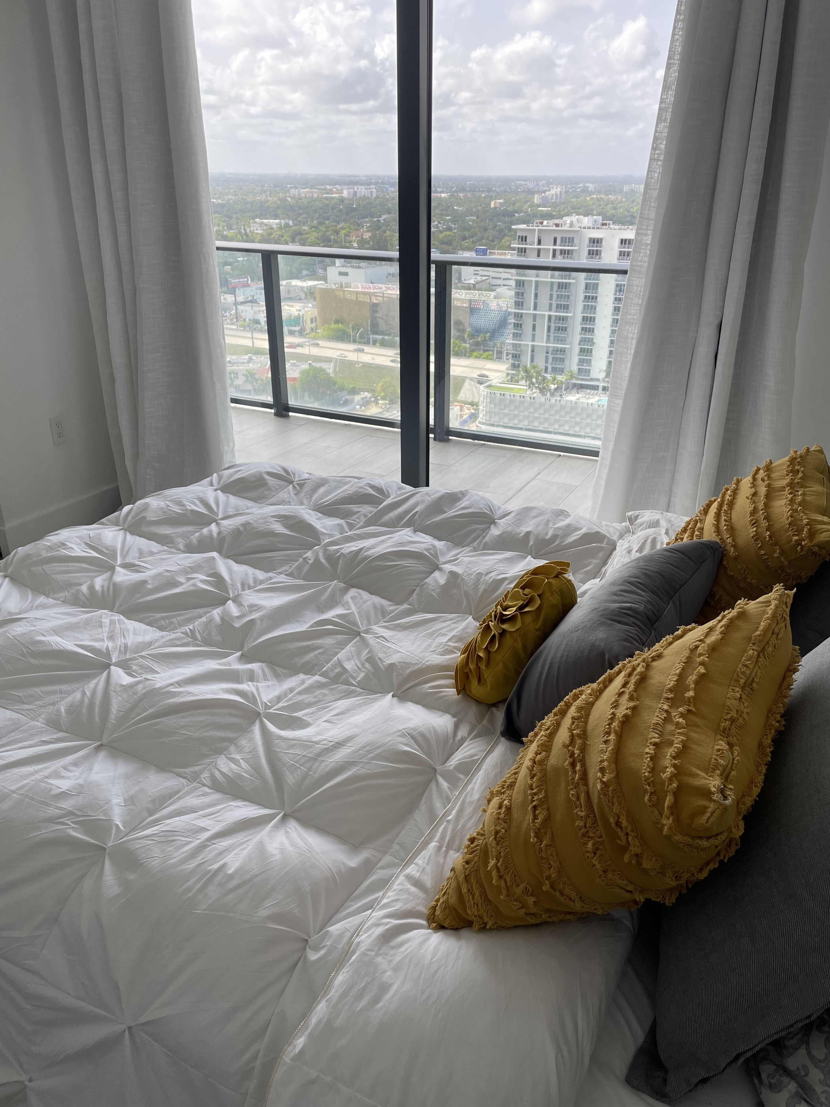 Quarto com uma cama grande, roupa de cama branca e dois travesseiros decorativos.