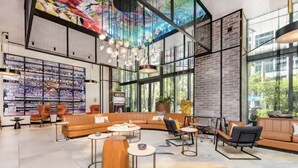 Eine geräumige Lobby mit modernem Design, ausgestattet mit einer großzügigen Sitzecke, einer Wand mit gerahmten Bildern und großen Fenstern für viel Tageslicht.