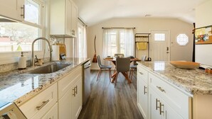 A kitchen with white cabinets, a granite countertop, and a dining area with a table and chairs. - Catskill Kaaterskill  Cabin Hot Tub FirePit Sauna (Lanesville)