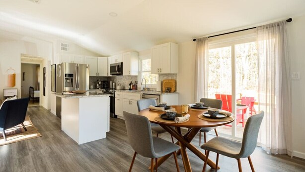 A modern kitchen with white cabinets, stainless steel appliances, and a dining area with a wooden table and chairs. - Catskill Kaaterskill  Cabin Hot Tub FirePit Sauna (Lanesville)