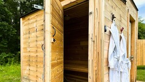 A wooden sauna with a door open, revealing an interior. There are towels hanging on the wall.