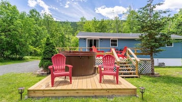 Relax in a tranquil setting with a hot tub and Adirondack chairs on a deck surrounded by lush greenery.