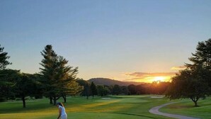 Un terrain de golf où un seul golfeur, vêtu de blanc, se trouve au milieu d’arbres, sous un ciel dégagé.