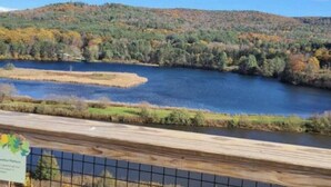 Une vue d’un lac entouré d’arbres aux couleurs automnales, avec une terrasse en bois au premier plan.