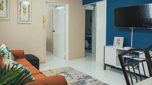 Un salon comprenant un canapé, une table basse, un téléviseur et une porte donnant sur une autre pièce.