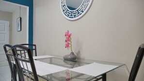 A dining table with chairs, a vase with flowers, and a wall-mounted mirror. - Yhavarees Comfy Oasis 2-Bed Aprt- Central & Secure (Kingston)