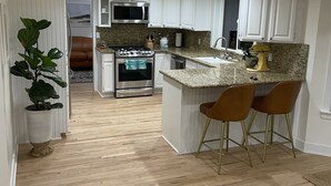 A modern kitchen with white cabinets, a granite countertop, and a built-in oven. There are two bar stools and a potted plant. - Beachy Home in Provo. Large deck with builtin hot tub, Fire pit, Palapa (Provo)