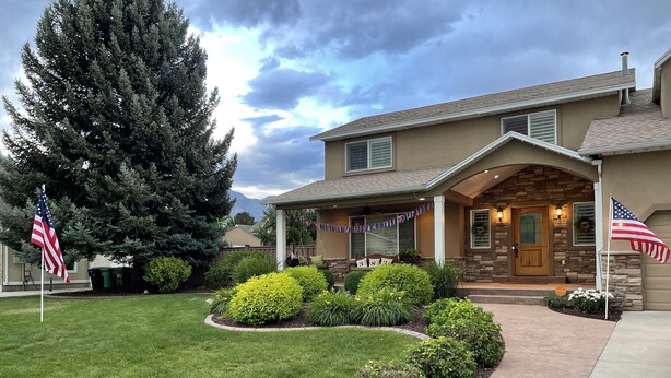 A two-story house with a stone facade, a front porch, and a well-maintained lawn. - Beachy Home in Provo. Large deck with builtin hot tub, Fire pit, Palapa (Provo)