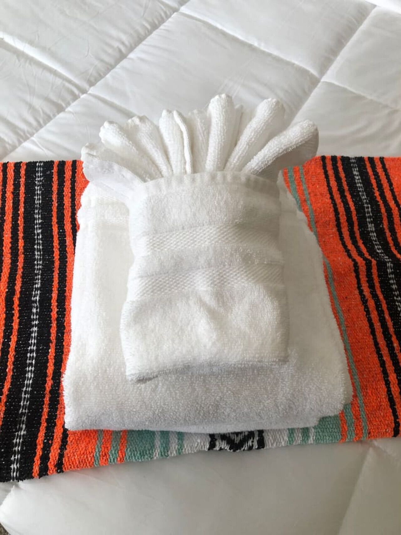 Una toalla blanca doblada cuidadosamente sobre una cama con un almohadón a rayas.