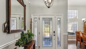 A foyer with a white door, a large mirror, a chandelier, a dining area with wooden chairs, and a potted plant. - TROPICAL RETREAT WITH PRIVATE HEATED POOL-TAMPA BAY. (New Port Richey)
