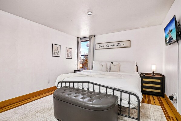 A bedroom with a bed, a bedside table, a television, and a window with curtains.