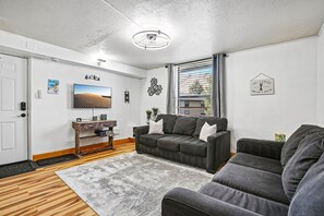 A living room with a grey sofa, a wooden coffee table, a flat-screen TV, and a decorative wall piece.