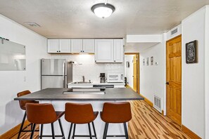 A modern kitchen with white cabinets, stainless steel appliances, a central island with bar stools, and a wooden floor.