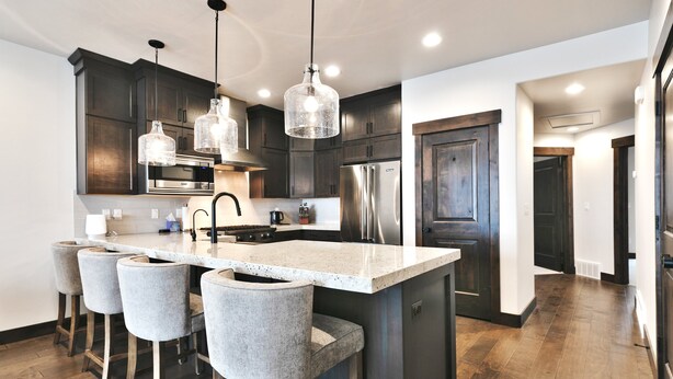 A modern kitchen with dark wood cabinets, stainless steel appliances, a large island with bar stools, and pendant lighting.