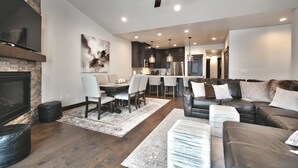 A modern living room with a fireplace, leather sofa, dining area, and kitchen in the background.