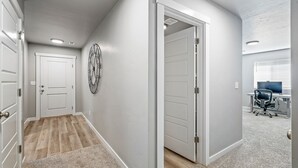 A hallway with a wooden floor, white walls, and a door leading to a room with a desk and chair. - Cheerful  NEW Executive Home with office-Meridian (Meridian)