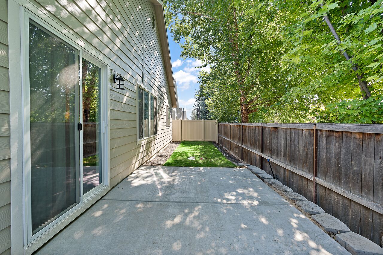 Un patio trasero residencial con valla de madera, un sendero de concreto y un pequeño césped.