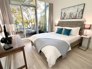 A modern bedroom with a large bed, a cityscape painting, and a view of trees through the window. - Solace in the City-Downtown, Close to Everything, Private Garden Patio (Victoria)