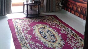 Ein Zimmer mit Buddha-Fresko, einer Steinsandsteinwand, einem gemusterten Teppich und einem kleinen Tisch mit einer Pflanze.