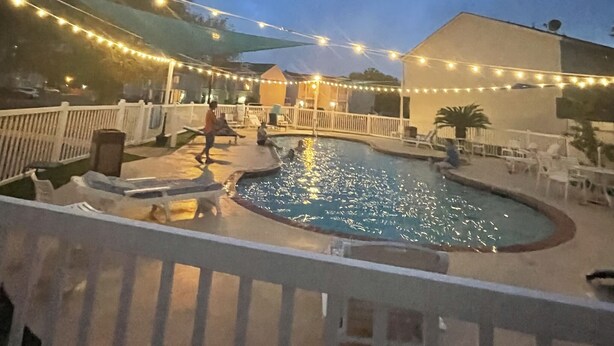 Area piscina con luci a stringa, terrazza recintata e posti a sedere esterni.