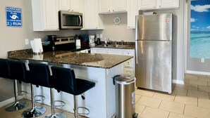Cucina con mobili bianchi, frigorifero in acciaio inossidabile, forno a microonde e macchina da caffè. Un cartello a parete indica il piano di evacuazione per uragani.