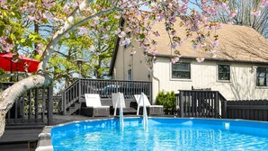 Une piscine avec des chaises longues, une terrasse en bois et une maison en arrière-plan.