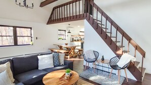 Un salon moderne avec un escalier, un coin repas et une cuisine en arrière-plan.
