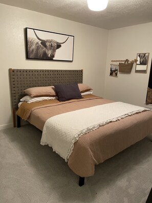 A bedroom with a wooden headboard, a large bed with a quilted white and brown bedspread, and a framed picture of a bull on the wall. - 5 bedroom charming modern cottage (Meridian)
