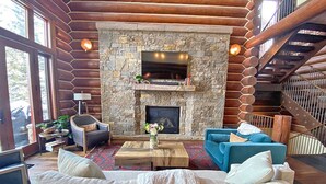 A cozy living room with a stone fireplace, wooden walls, and a blue sofa. - Luxury Townhome-Bike/Hike-Out the Door Access-Private Hot Tub-3 King Bed En Suite-Bunk Room (Mountain Village)