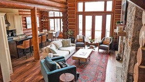 A log cabin interior with a dining area, a living room with a sofa and armchairs, and a stone fireplace. - Luxury Townhome-Bike/Hike-Out the Door Access-Private Hot Tub-3 King Bed En Suite-Bunk Room (Mountain Village)