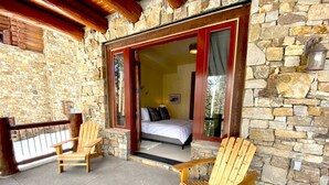 A stone exterior with a wooden deck, two Adirondack chairs, and a bed visible through an open door. - Luxury Townhome-Bike/Hike-Out the Door Access-Private Hot Tub-3 King Bed En Suite-Bunk Room (Mountain Village)