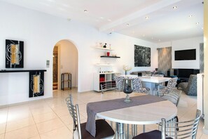 A spacious living area with a round dining table, modern chairs, and a kitchen in the background.